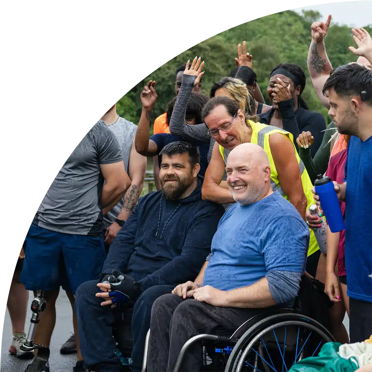A diverse group of people, including individuals using wheelchairs smiling and celebrating together outdoors after a community or fitness event.