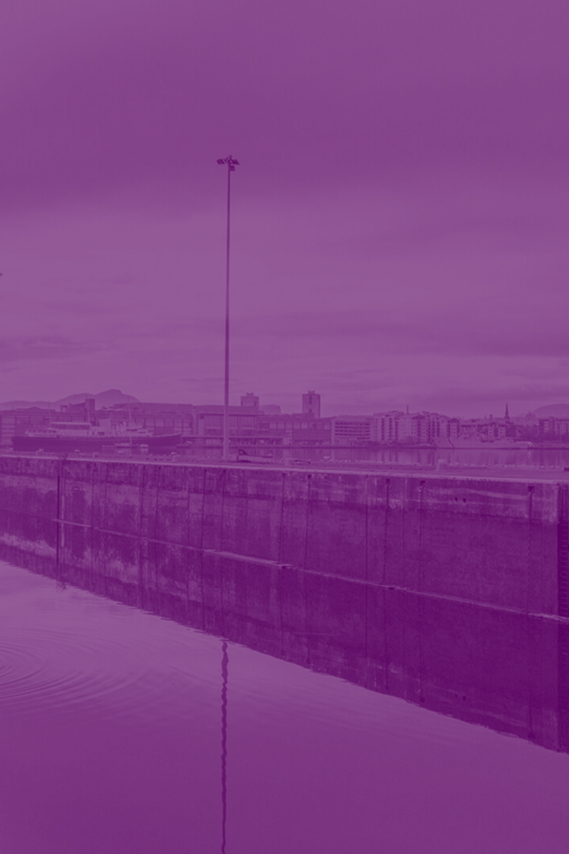 Meteorological mast with weather instruments on a concrete harbor wall overlooking urban waterfront under cloudy sky
