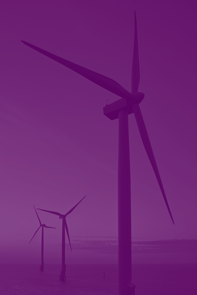 Silhouettes of offshore wind turbines against purple and pink sunset over calm ocean