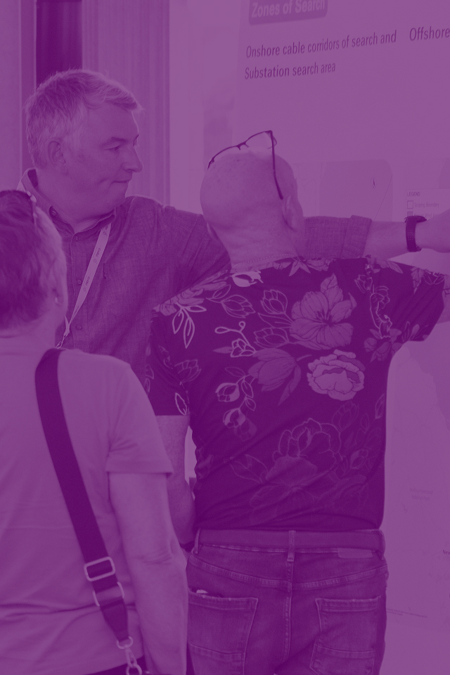 Three men examining an offshore wind development map showing zones of search and cable corridors at a public event