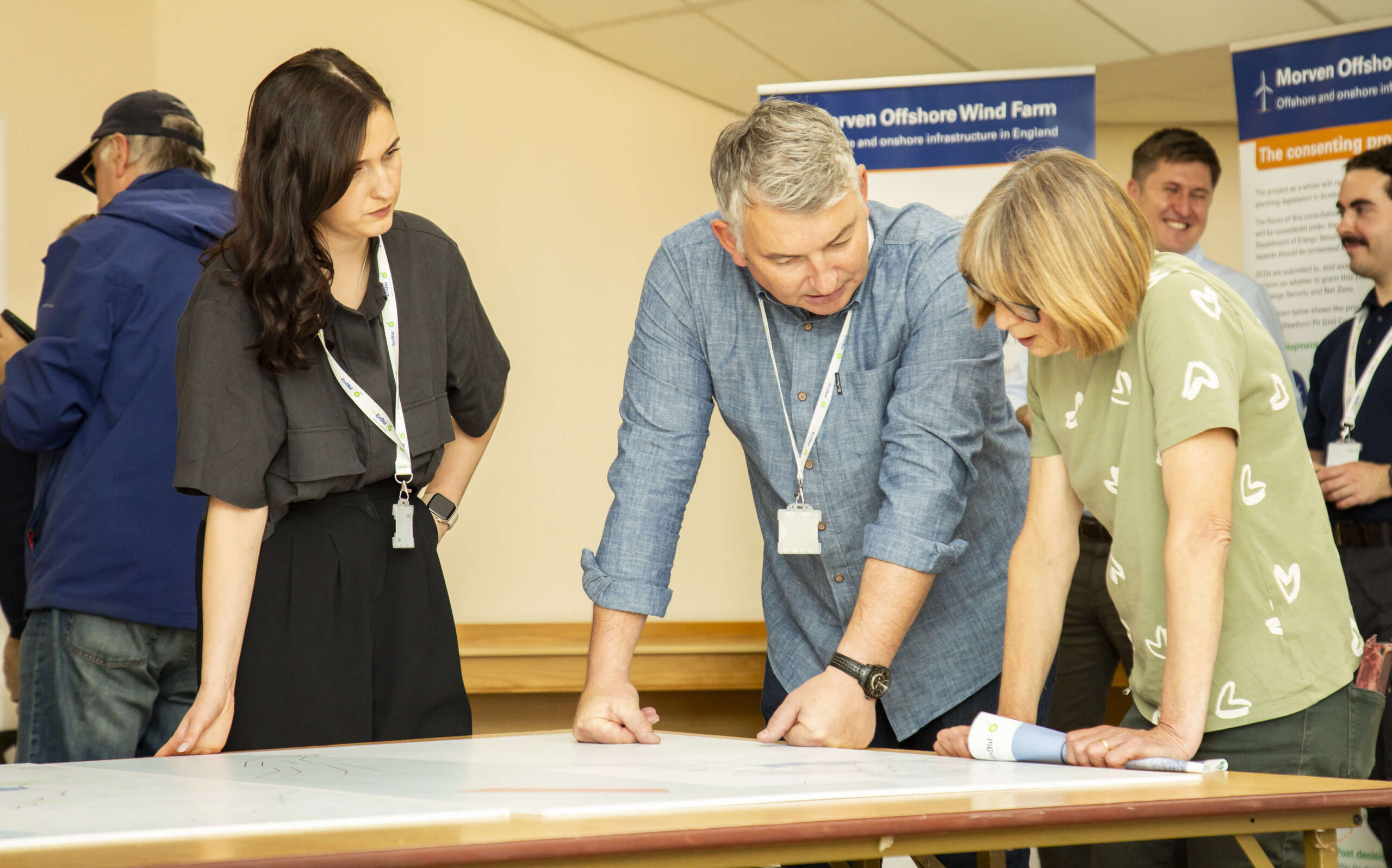 Three people discussing plans over a table with Morven Offshore Wind Farm banners in the background