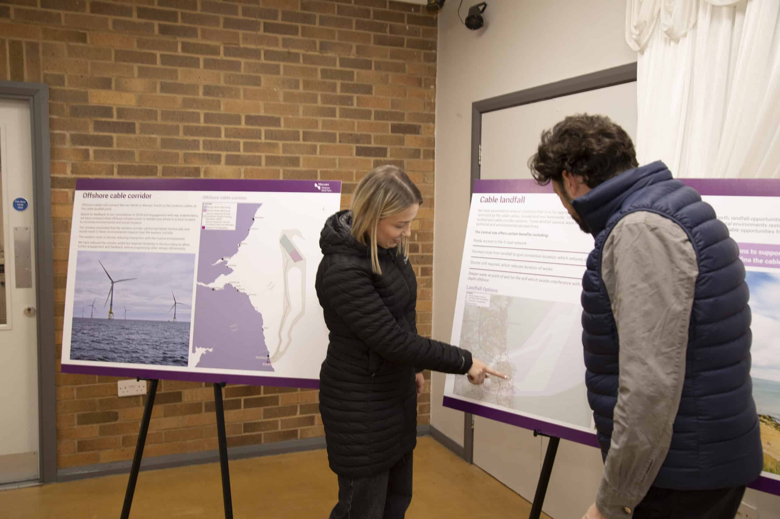Two people discussing maps on presentation boards indoors