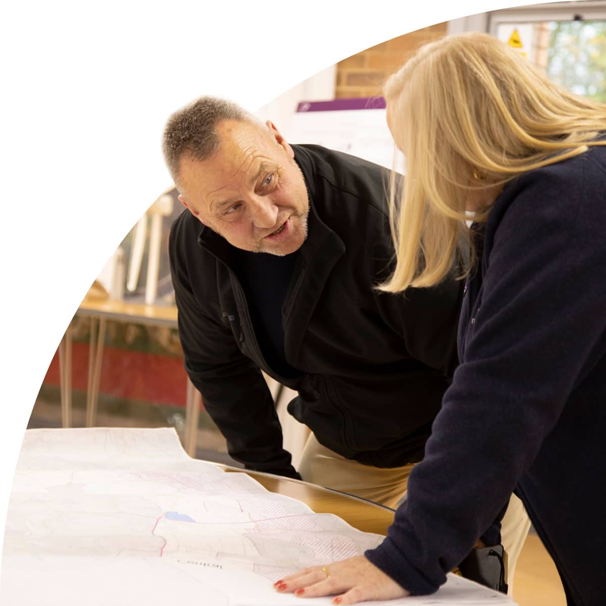 Two people discussing a large map on a table indoors