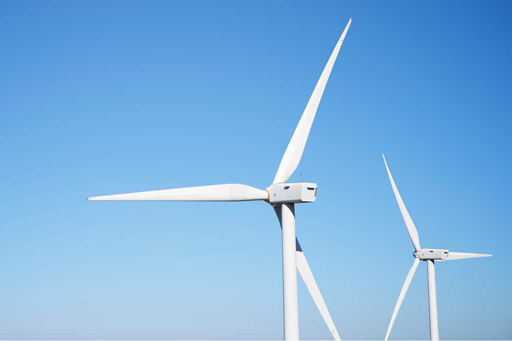 Two white wind turbines against a clear blue sky