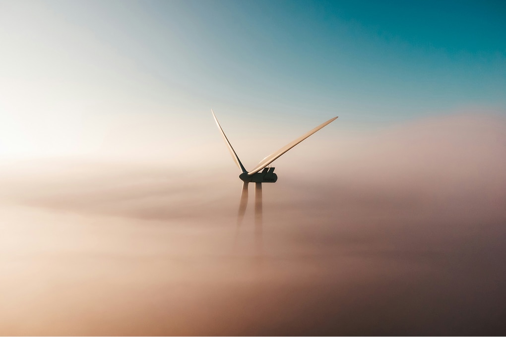 Wind turbine blades above dense fog under a clear sky