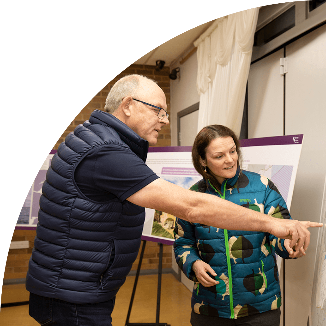 Two people discussing and pointing at information displayed on a board indoors